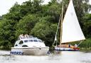 A hire cruiser passes a yacht in the Norfolk Broads